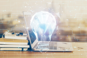 Computer on desktop in office with bulb icon hologram. Multi exposure. Concept of idea.