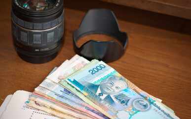 Camera lens, foreign money and aircraft boarding pass on a wooden table. Tourism, vacation, travel photography equipment.