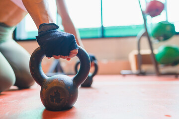 Kettlebell on the red floor held in hand of athlete in blurry at the background.