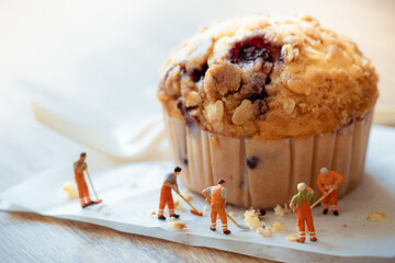 Miniature people worker cleaning muffin food cake on wooden table use for background sweet food...