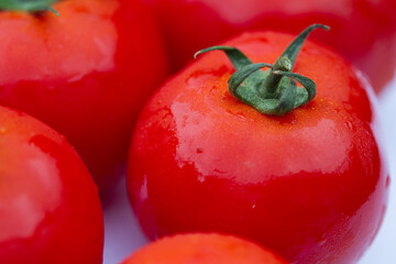 Details of a red tomato with green stipe and other blurry tomatoes in the background