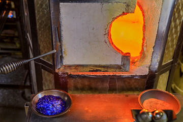 Glass blowing furnace and table with crushed glass and tools at a glass maker's workshop set up for the process