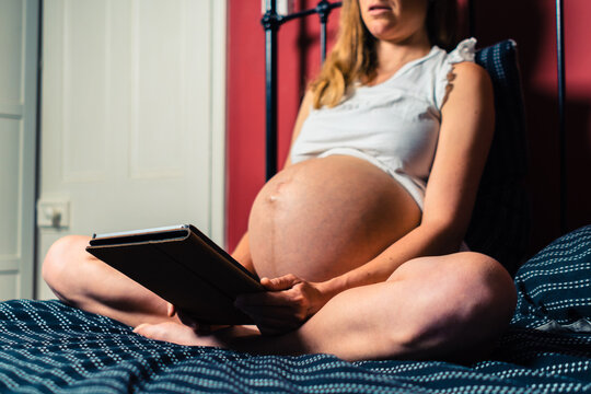 Young pregnant woman using tablet in bed