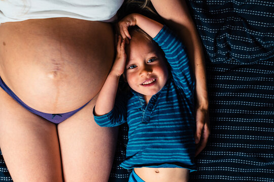Little boy lying next to his pregnant mother in bed