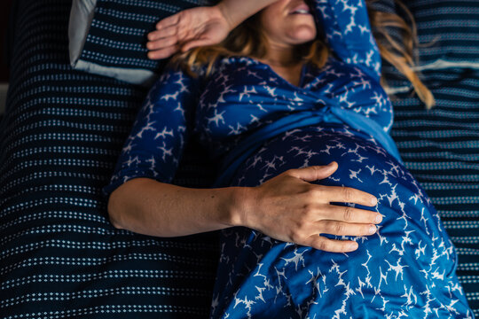 Pregnant woman in gown lying on bed with hand on her belly