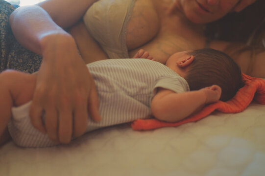 Young mother breastfeeding her newborn baby on bed