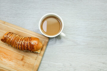 A loaf of red bean bred on chopping board and a cup of coffee on wooden table 
