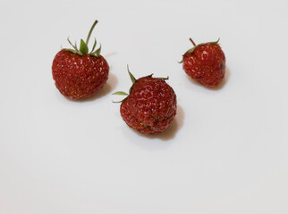 Three berries. On a white porcelain plate lies strawberries. Red berries with green leaves. Ripe fruits. Great dessert. Freshly picked fruits. The background is only white, a plate without patterns.