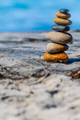 Fototapeta na wymiar Stacked stones/ pebbles naturally balanced on beach sand on a sunny summer day. Rock Zen stack balancing. Meditation symbol of peace and harmony.