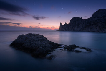 Quiet evening on the seashore. Picturesque cliffs, calm expanse of the sea, beautiful sunset sky with first stars. Peace, solitude, mediation in silence. Copy space on water surface. Long exposure.