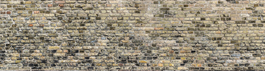 An old textured brick wall with hues of gray, brown, tan and white