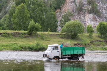 Small truck (UAZ) cross Belaya river on the background of beautiful Ural landscape. Bashkortostan, Ural, Russia.