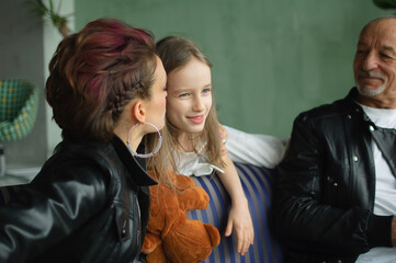Family portrait of adult daughter, little granddaughter and senior grandfather in loft room with houseplants. Man and woman are wearing black leather jackets in punk style, generation concept