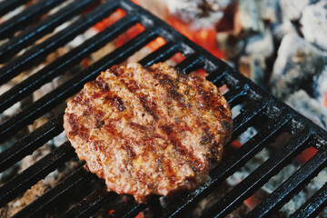 Meat cotlet for burger cooking on grill, barbeque with opened coals in cafe.