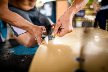 close-up of surfboard on which man's hands carefully attaches fins