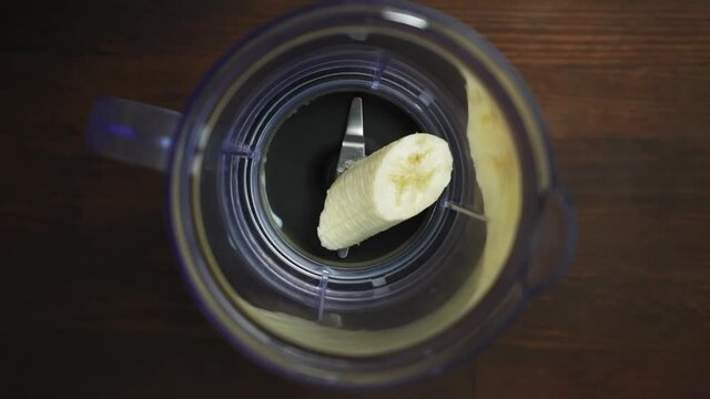 Man drop slices of banana in to a blender. Man preparing banana pure in the blender for a morning milk shake. Blander on dark wooden table. Prores 422. 