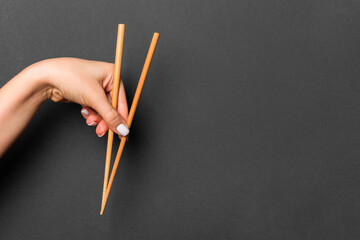 Wooden chopsticks holded with female hands on black background. Ready for eating concepts with empty space