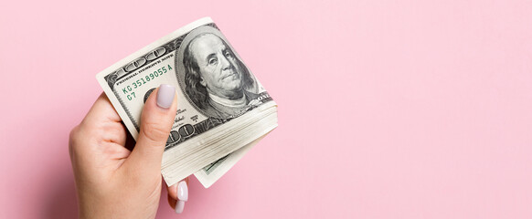 A pack of one hundred dollar bills in female hand on colorful background. Salary concept with copy...