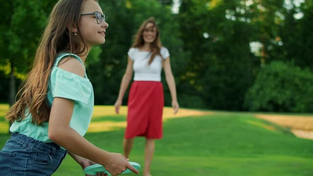 Woman throwing frisbee disk to daughter in park. Girl catching frisbee plate