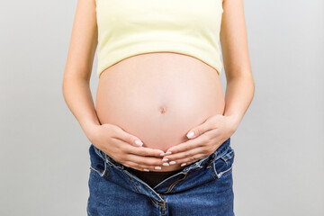 Close up of naked pregnant woman's belly wearing opened jeans at colorful background with copy space. Pregnancy concept