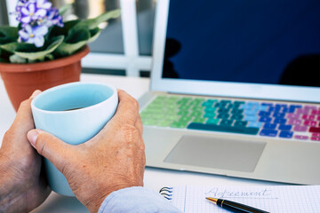 Close-up of senior woman hands with a coffee cup, laptop on the desk - smart worker due to coronavirus