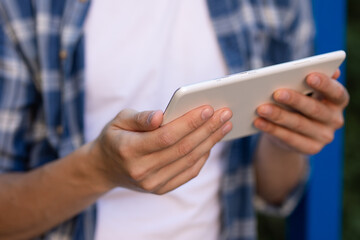 tablet in the hands of a guy in a blue checked shirt, close-up
