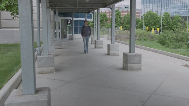 High quality 4k video of a young men who is walking outside on the street to to from parking lot on the train station. Canada GO train and bus station. Handsome men carrying backpack