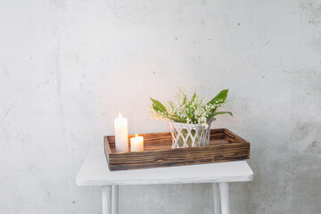 lily of the valley in vase with burning candles on background old white wall