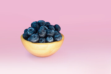 Blueberries in a wooden bowl on pink background