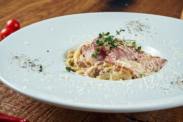 Homemade Italian carbonara pasta with bacon and parmesan in a white plate on a wooden background