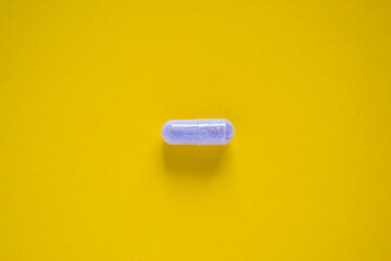 One white medical pill on yellow background