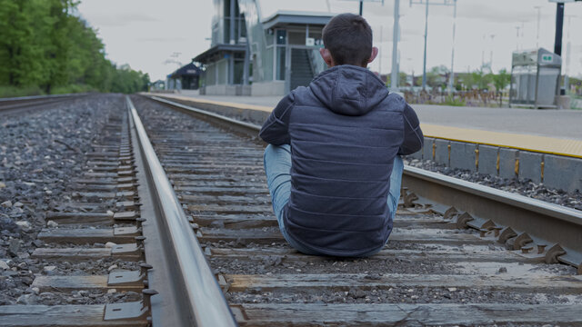High quality picture of a young man sitting on a railway station and looking to the horizont. Depressed person sitting on a railway.