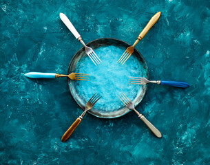 Colored set of kitchen plate with forks on a turquoise blue background. Top view