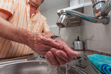 Older man washing his hands in the kitchen before cooking to prevent coronavirus and other contagious diseases. Selective focus.