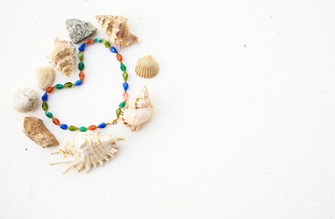 Set of seashells, pearls and stones in form heart on a  white background. Place for inscription. Postcard.