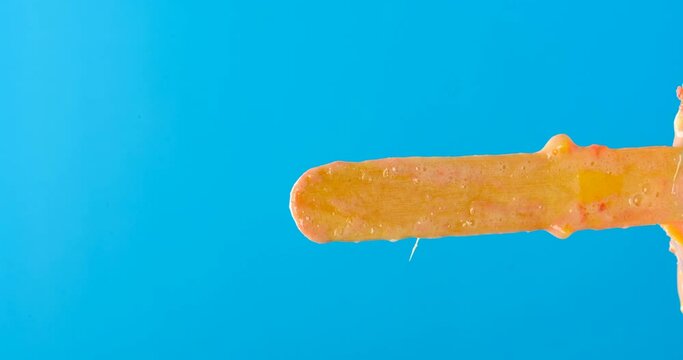 fresh orange flavor popsicle melting timelapse on a blue background please rotate it at 90 degrees to get a vertical composition