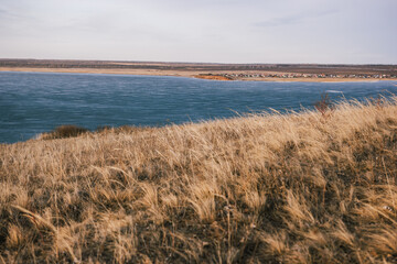 
View from a hill with dry grass to a frozen lake without snow