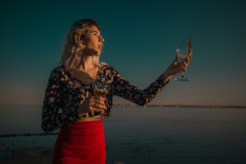 young curly blonde fooling around with glasses in hand on a background of sky and sea