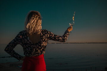 young curly blonde fooling around with glasses in hand on a background of sky and sea