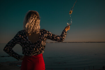 young curly blonde fooling around with glasses in hand on a background of sky and sea