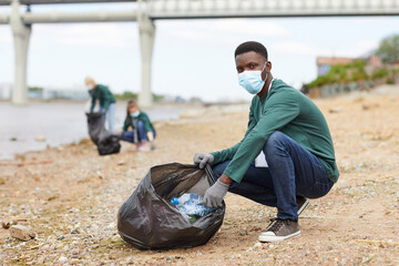 Portrait of African young man in protective mask looking at camera while putting the garbage in the...
