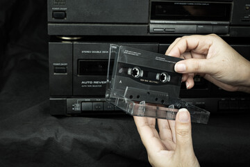 Obraz premium Close up women hand holding a cassette tape compact at old played audio tape background