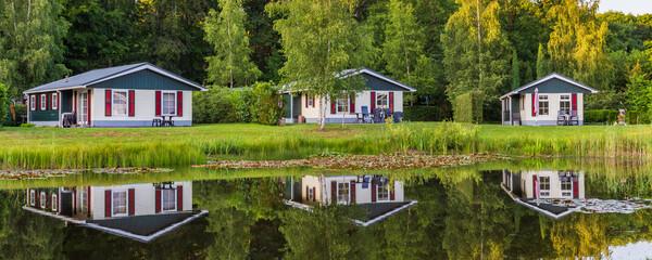 Panorama with row of colorful wooden vacation home reflected in a pond at recreation park in the...