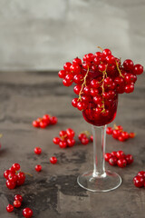 Fototapeta na wymiar Red currant in a shot glass, the rest is scattered around it on a gray textured background