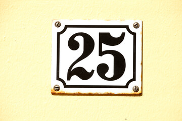 Altes weisses Hausnummernschild Nummer Fünfundzwanzig aus metall an einer gelben Hauswand