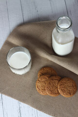 cookies, a bottle and a glass of milk on canvas napkin on white wooden background flat lay