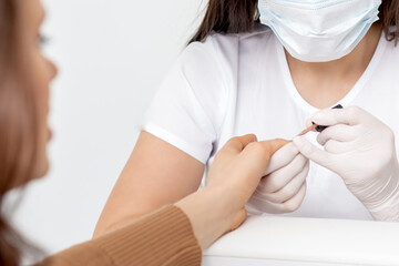 Manicurist in protective mask painting female nails with nail polish in manicure salon.