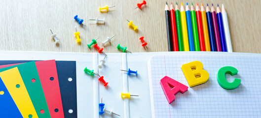 Colorful composition of vibrant color school supplies: colored pencils, papers, pens and english letters on the withe wooden background. Banner. Flat lay. Back to school and education concept.