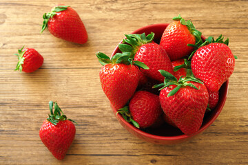 Ripe large strawberries in a red bowl on a wooden table