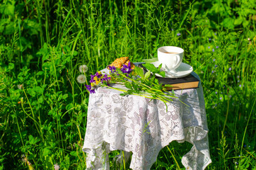 A Cup of green tea with a mint leaf, flowers, and a book on a table in the garden. Evening tea with cookies. Summer village concept. High quality photo